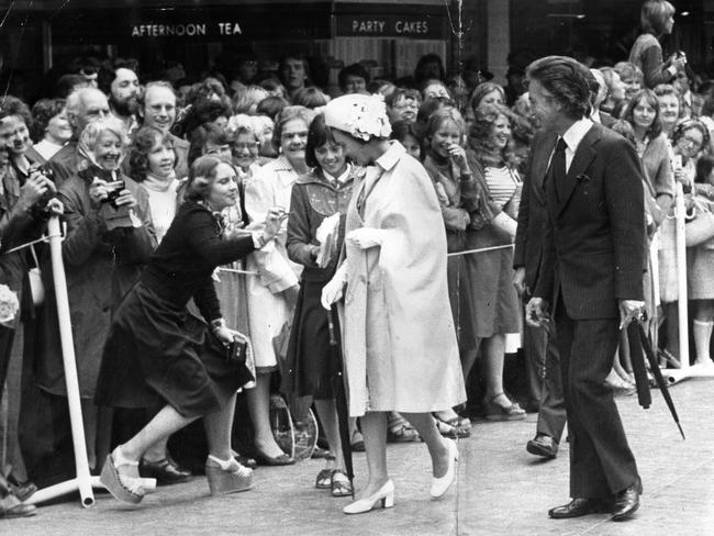 A woman steps out of the barricade on Rundle Mall to give a gift to the Queen whilst curtseying.