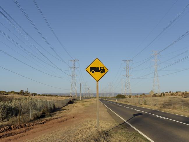 A sign indicating "truck crossing or entering" stands along a road as power lines hang from transmission towers on Torrens Island, South Australia, on Monday, April 2, 2018. A plan byÃÂ Tesla Inc.ÃÂ to build the world's largest virtual power plant may be in jeopardy after the South Australian political party that championed the deal was ousted from government, setting up a potential retreat from ambitious renewableÃÂ energyÃÂ targets. Photographer: Carla Gottgens/Bloomberg via Getty Images