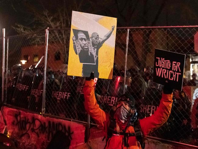 A demonstrator holding a poster of George Floyd and sign reading "Justice for Wright" in front of a line of police officers outside the Brooklyn Center police station. Picture: AFP