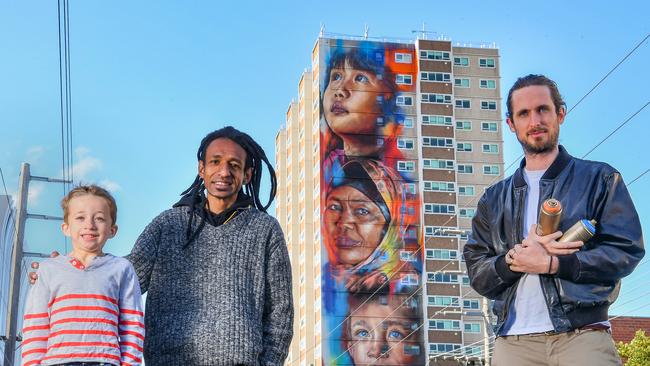 Arden Watson-Cropley and Yulius Taime with street artist Matt Adnate whose high-rise mural features the faces of four residents of a public housing estate in Wellington Street, Collingwood. Photo: Jason Edwards