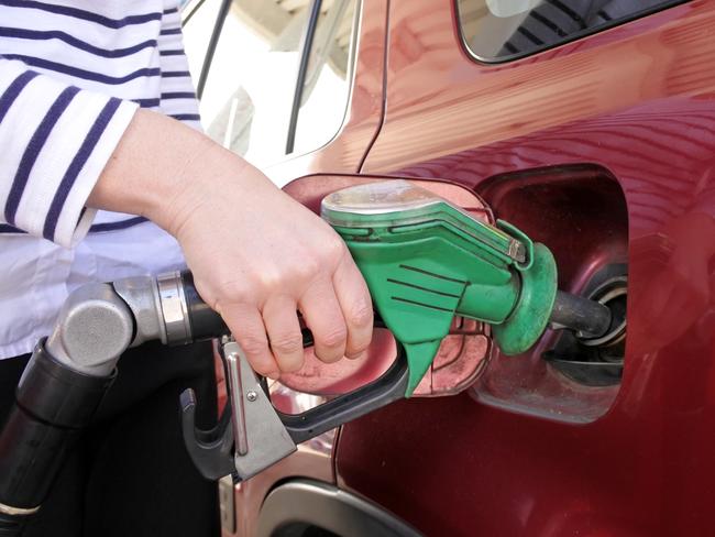 Woman using a gas pump nozzle fulling a car in a gas station.