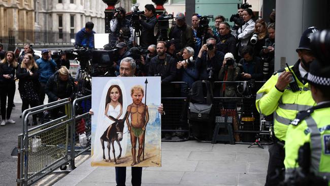 Political satire artist Kaya Mar holds a painting portraying Prince Harry, Duke of Sussex, and his wife Meghan, Duchess of Sussex, as members of the media gather outside the Royal Courts of Justice in central London.