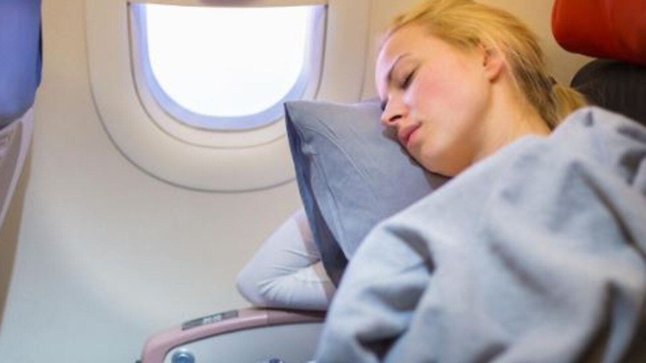 A woman opts to keep her seat upright and lean sideways on a pillow to snooze instead of reclining her seat. Picture: iStock