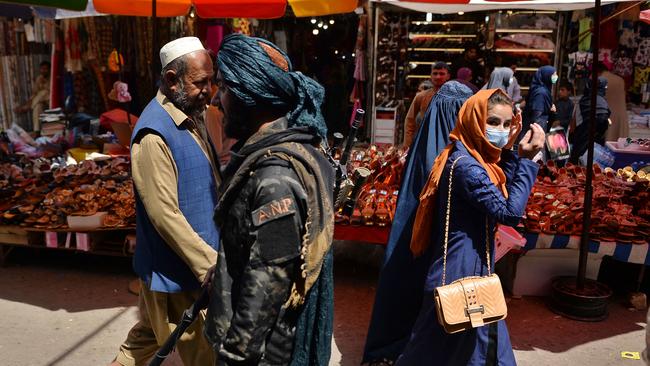 A Taliban fighter walks past shoppers along Mandawi market in Kabul. Picture: AFP