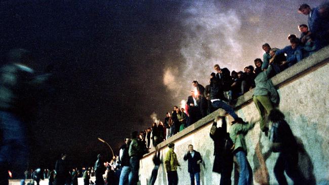 East German citizens climb the Berlin Wall at the Brandenburg Gate after the East German border opens.