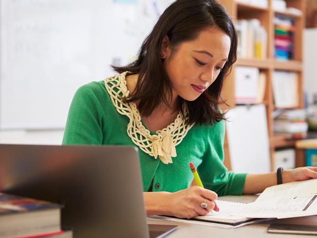 Female Asian teacher at her desk marking studentsâ?? work