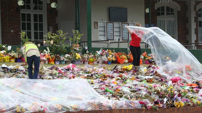 Red Cross volunteers cover the floral tributes to those who lost their life at Dreamworld with plastic to protect them from rain. Picture by Scott Fletcher