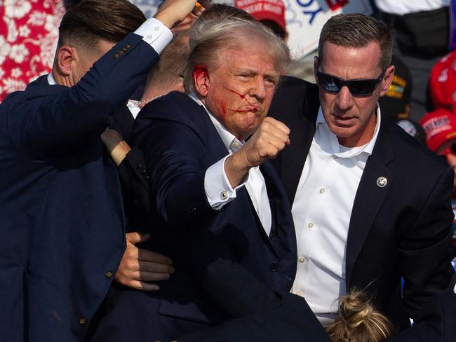 US Republican candidate Donald Trump is seen with blood on his face surrounded by secret service agents as he is taken off the stage at a campaign event at Butler Farm Show Inc. in Butler, Pennsylvania, on July 13, 2024. Trump was hit in the ear in an apparent assassination attempt by a gunman at a campaign rally on Saturday, in a chaotic and shocking incident that will fuel fears of instability ahead of the 2024 US presidential election. The 78-year-old former president was rushed off stage with blood smeared across his face after the shooting in Butler, Pennsylvania, while the gunman and a bystander were killed and two spectators critically injured. (Photo by Rebecca DROKE / AFP) / QUALITY REPEAT