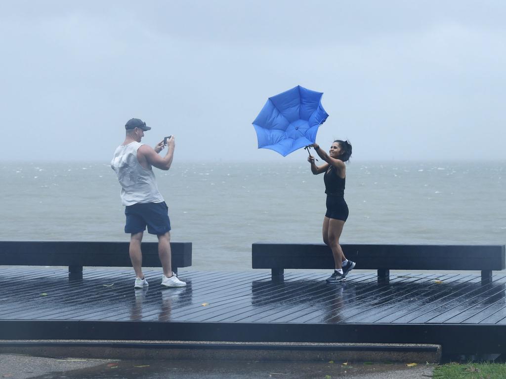 Garth Howarth takes a photo of Davina Young before her umbrella blows inside out on the Cairns Esplanade at high tide as Tropical Cyclone Jasper heads towards the Far North Queensland coast. Picture: Brendan Radke