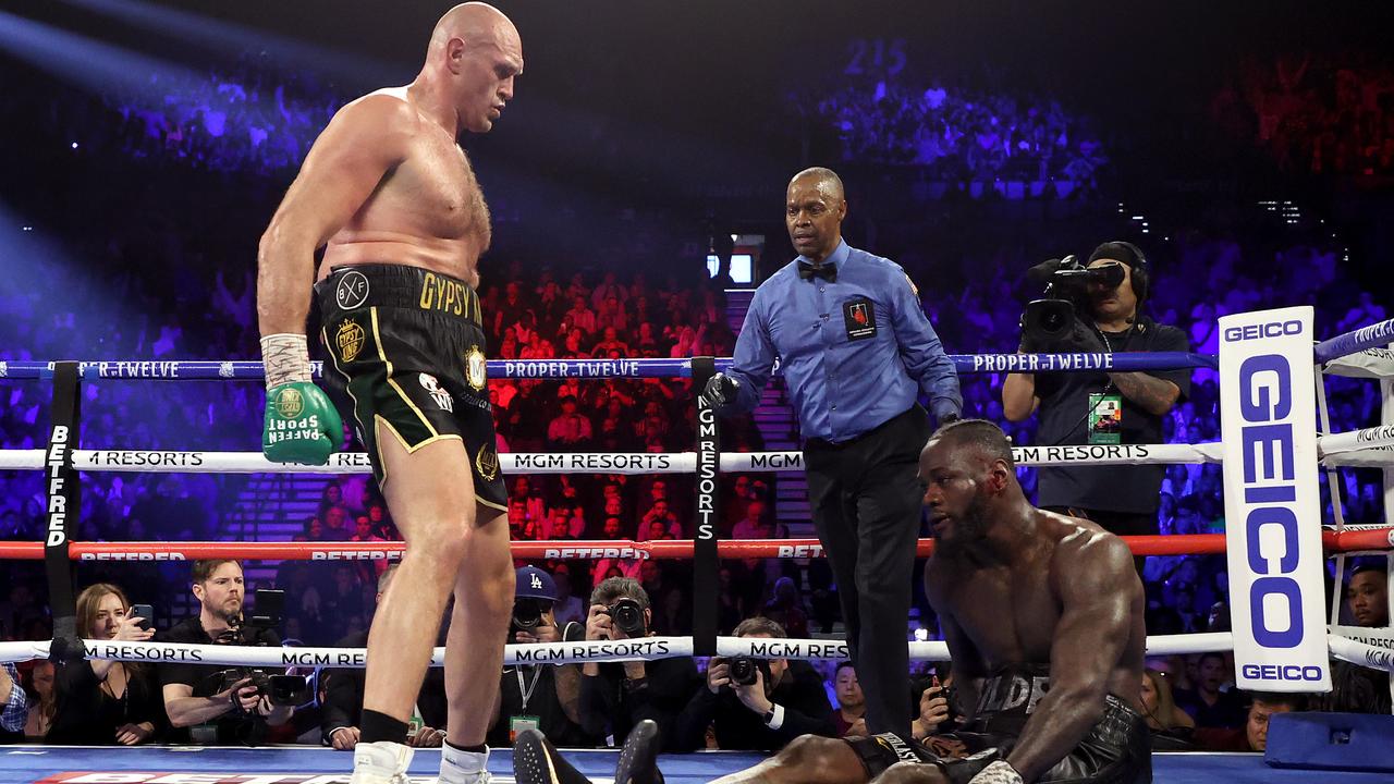 Tyson Fury looms over Deontay Wilder after knocking him down in the fifth round.