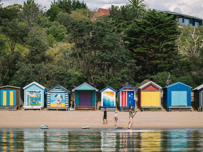 Mornington Peninsula, VictoriaOn the scenic Mornington Peninsula in Victoria, people stroll along the sandy beach and paddle board in the calm waters. In the background, colourful heritage bathing boxes, nestled below lush trees, add a vibrant touch to the landscape. These iconic structures offer perfect summer shelters for enthusiastic beachgoers, enhancing the charm of the coastal scene.Photo - Tourism AustraliaEscape 14 July 2024one time use in Escape