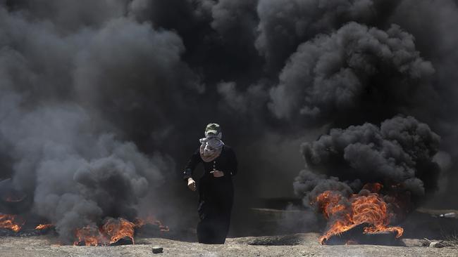 A Palestinian woman walks through black smoke during a protest on the Gaza Strip's border with Israel.