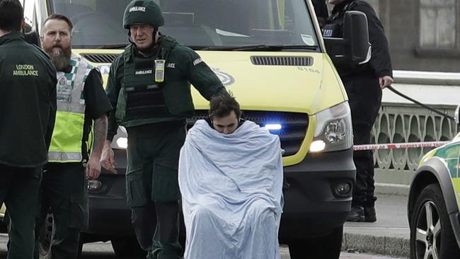 An injured man sits covered with a blanket as emergency services staff provide medical attention to injured people on the south side of Westminster Bridge. Picture: AP