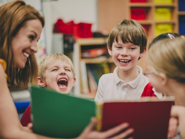 Teacher is sitting in the classroom with her primary school students, reading a story to them.