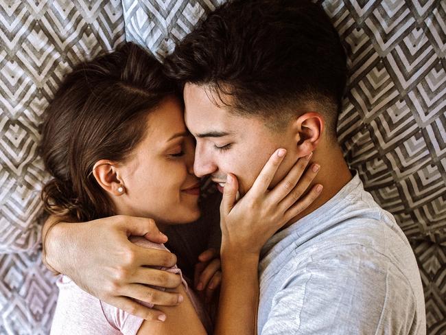 Young couple in love lying on bed at home and cuddling, embracing and enjoying weekend together