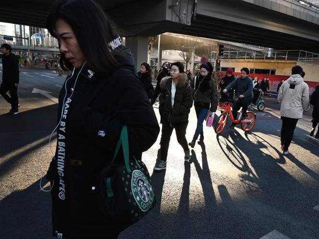 Commuters walk across a road in Beijing's central business district on January 21, 2019. - China's economy grew at its slowest pace in almost three decades in 2018, losing more steam in the last quarter as it battles to quell massive debt and a US trade war, official data showed on January 21. (Photo by GREG BAKER / AFP)