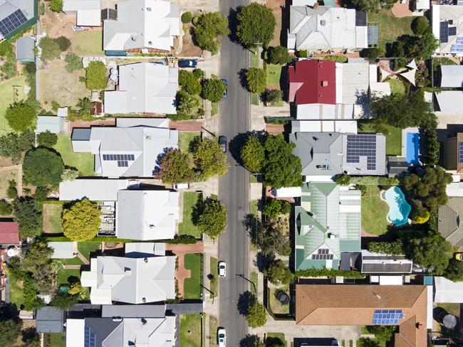 Aerial view of houses and properties in a suburban street in Adelaide's inner northern suburbs: tree-lined with different roof types, varying neatness and with some solar panels evident. Also swimming pools, trampolines, lawns, gardens, driveways.