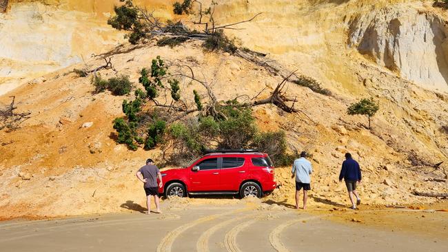 Onlookers with the car partially buried by a Rainbow Beach sand slide on Wednesday, August 3, 2023.