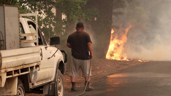 A Woodside resident battles a fire as it crosses Ridge Road at Woodside in the Adelaide Hills in Adelaide, Friday, December 20, 2019. Two bushfires are burning out of control around the Adelaide Hills, prompting emergency warnings from the Country Fire Service. (AAP Image/Kelly Barnes) NO ARCHIVING