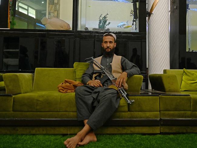 A Taliban fighter sits inside the mansion as exotic fish glide above him in giant fish tanks. Picture: AFP