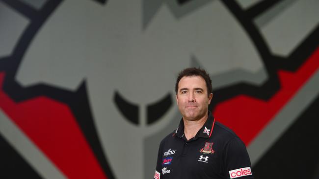 Essendon coach Brad Scott in front of the Bomber logo.