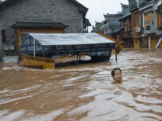 A woman makes her way through floodwaters in the ancient town of Fenghuang.