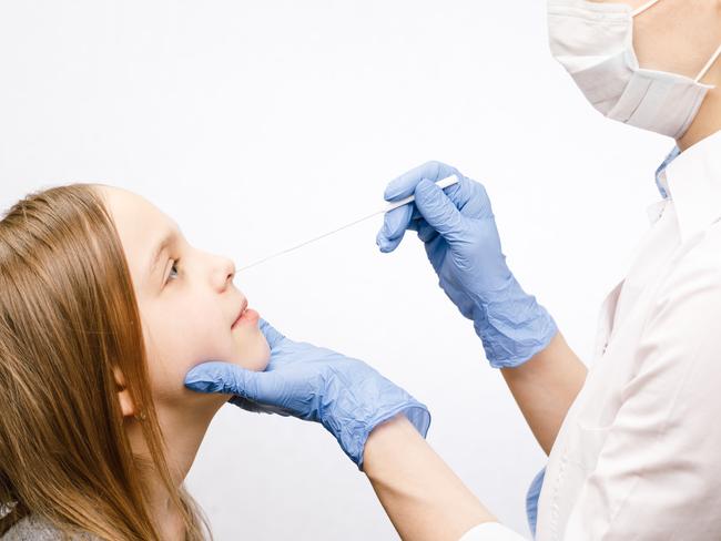 Pediatrician or doctor taking nasal mucus test sample from elementary age girl's nose performing respiratory virus testing procedure