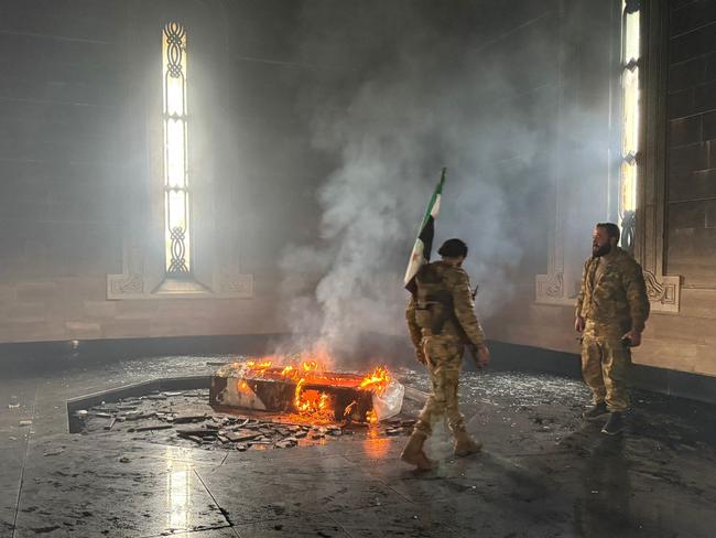 TOPSHOT - Rebel fighters stand next to the burning gravesite of Syria's late president Hafez al-Assad at his mausoleum in the family's ancestral village of Qardaha in the western Latakia province on December 11, 2024, after it was stormed by opposition factions. The father and predecessor of Syria's ousted president Bashar al-Assad died in 2000. (Photo by Aaref WATAD / AFP)