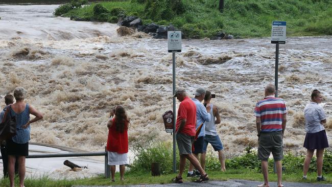 People gather to watch floodwaters in the Coomera River spill over the Oxenford Weir. Picture Glenn Hampson