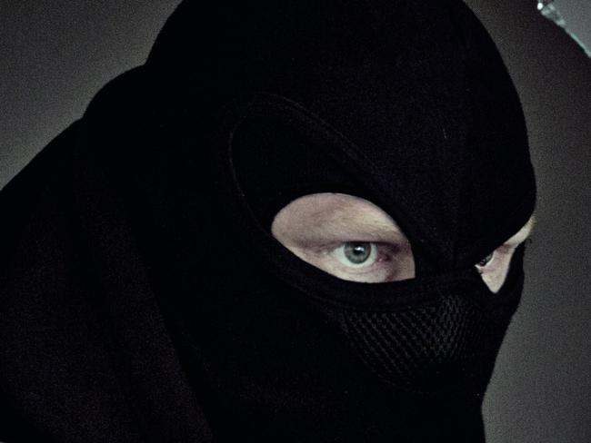 Man wearing a mask holding a gun through a broken window in a dark abandoned warehouse. istock