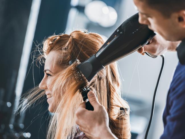 Young hairdresser drying customers hair with round brush at hair salon. Hairdresser generic