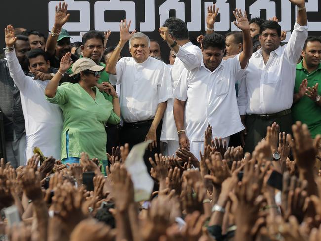 Sri Lanka's sacked prime minister Ranil Wickremesinghe, third from left in white shirt and black trousers, waves to his supporters along with law makers supporting him during a protest rally outside the prime ministers official residence in Colombo, Sri Lanka, Tuesday, Oct. 30, 2018. Thousands of supporters of wickremesinghe gathered in capital demanding president Maithripala Sirisena to convene the parliament immediately. Back drop in Sinhalese reads " Respect the mandate! Convene the parliament ! Democracy ". (AP Photo/Eranga Jayawardena)