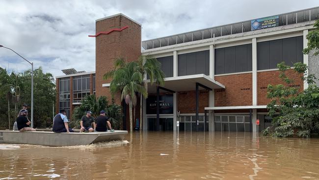 Police ride past the flooded Lismore council building. Picture: Stuart Cumming