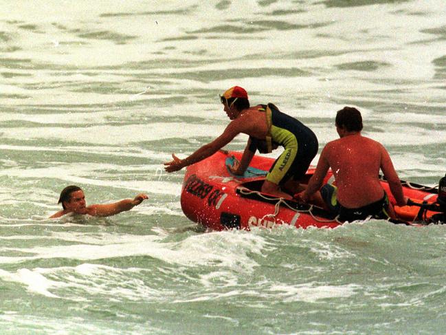 A swimmer is rescued by a lifesaver near rocks at Kirra beach.