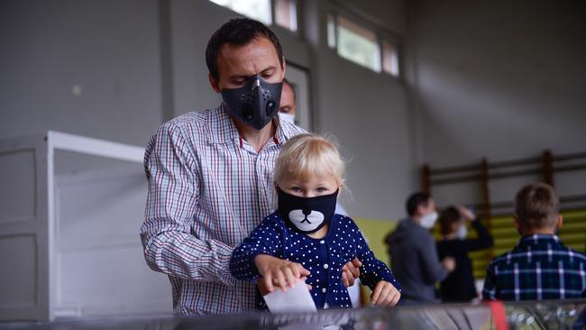 A man wears a protective face mask and holds a child while casting a ballot in Poland this month. Picture: Getty Images