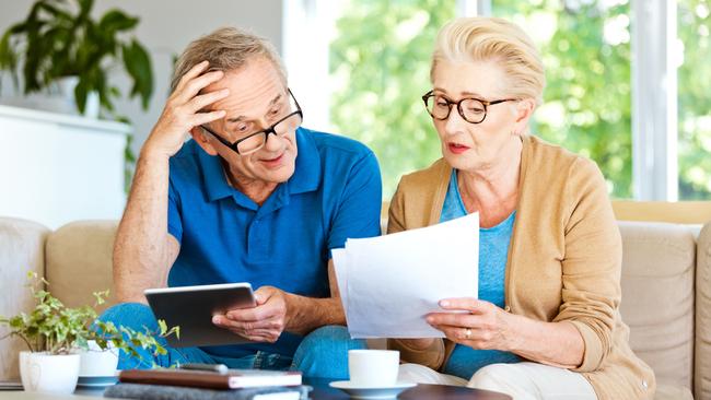 Worried mature woman and man sitting on sofa in living room at home. Senior couple watching bills and calculating monthly expenses.