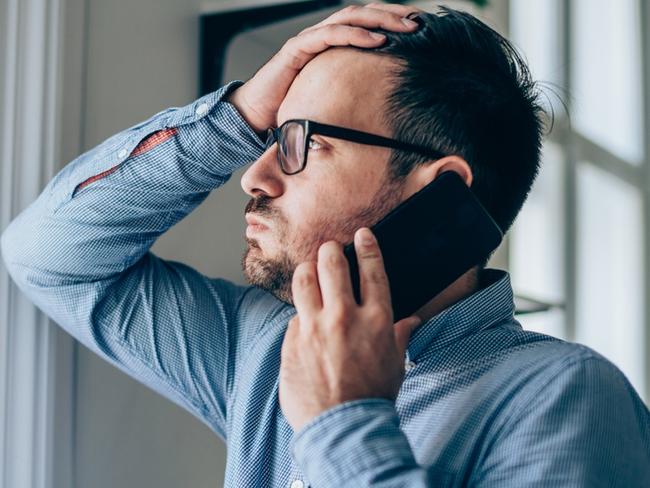 Worried businessman with hand on forehead talking on mobile phone in his office.