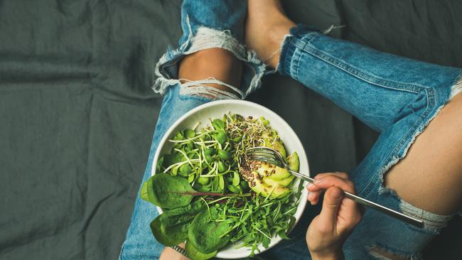 Green vegan breakfast meal in bowl with spinach, arugula, avocado, seeds and sprouts.