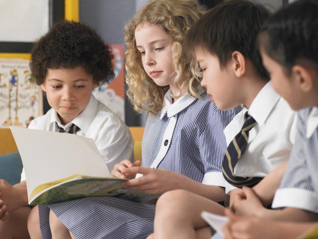 Row of elementary students reading book sitting in classroom