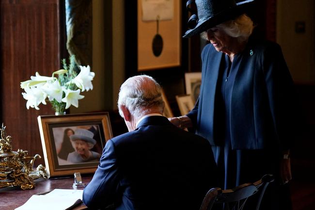 Camilla, Queen Consort (R) watches as Britain's King Charles III signs the visitors' book, alongside an image of his late mother Queen Elizabeth II, at Hillsborough Castle in Belfast.