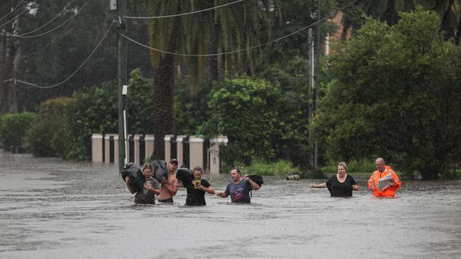 Local residents wade through floodwaters with their belongings in Sydney yesterday. Picture: Reuters