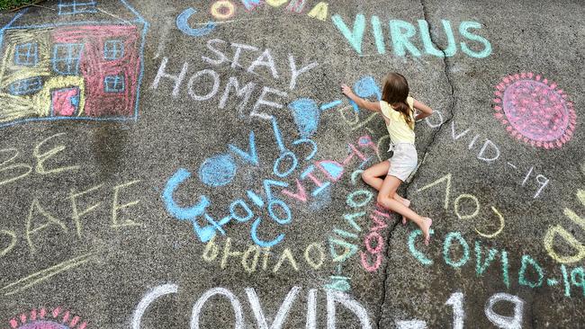 A young girl writes with chalk on her home driveway on the Gold Coast, as students prepare to remain at home to be schooled. Picture: AAP/Dave Hunt