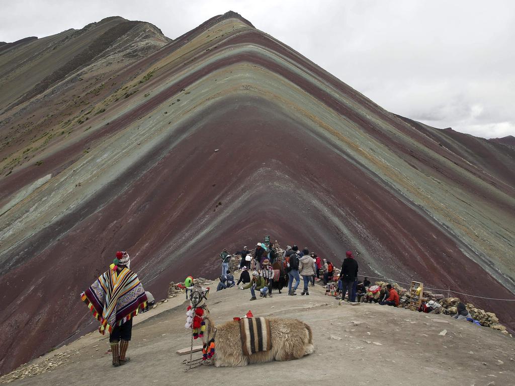 An Andean man rests with his llama as tourists take in the natural wonder of the mountain. Picture: AP/Martin Mejia