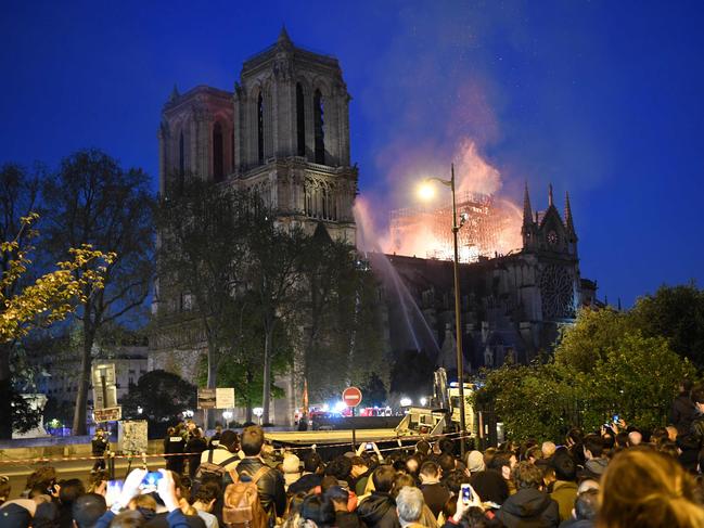 Crowds look on as flames and smoke billow from the roof at Notre-Dame Cathedral in Paris on April 15, 2019. - A fire broke out at the landmark Notre-Dame Cathedral in central Paris, potentially involving renovation works being carried out at the site, the fire service said.Images posted on social media showed flames and huge clouds of smoke billowing above the roof of the gothic cathedral, the most visited historic monument in Europe. (Photo by ERIC FEFERBERG / AFP)