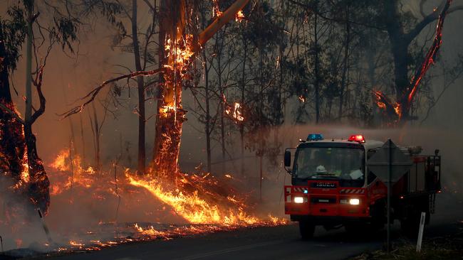 Bushfires on the South Coast of NSW. An RFS truck drives past trees alight in the hills behind Wyndham from the Big Jack Mountain fire in the Bega Valley. Picture: Toby Zerna