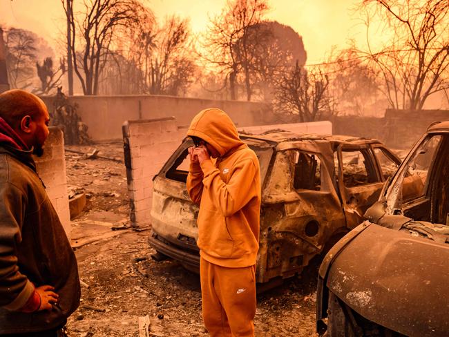 TOPSHOT - Lebron Jones (C) wipes his eyes while viewing his burned home during the Eaton fire in the Altadena area of Los Angeles county, California on January 8, 2025. At least five people are now known to have died in wildfires raging around Los Angeles, with more deaths feared, law enforcement said January 8, as terrifying blazes leveled whole streets, torching cars and houses in minutes. More than 1,000 buildings have burned in multiple wildfires that have erupted around America's second biggest city, forcing tens of thousands of people from their homes. (Photo by JOSH EDELSON / AFP)