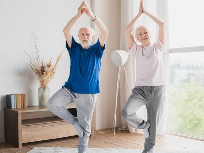 Fit sporty senior old elderly couple family spouses grandparents training stretching doing yoga exercises at home on lockdown together keeping balance on one foot.; active retirement generic