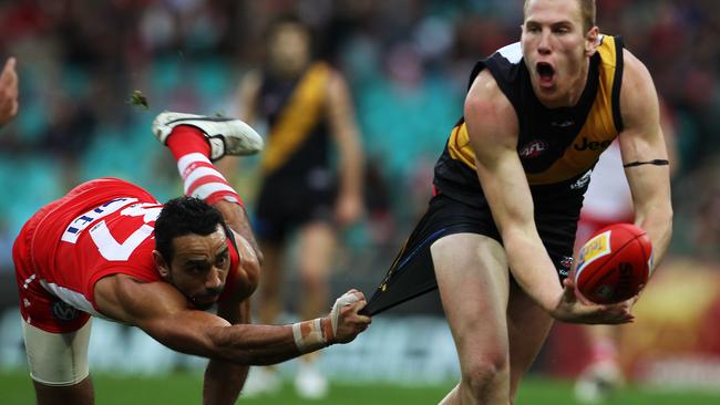 Andrew Browne handballs for Richmond while being tackled by Sydney’s Adam Goodes.