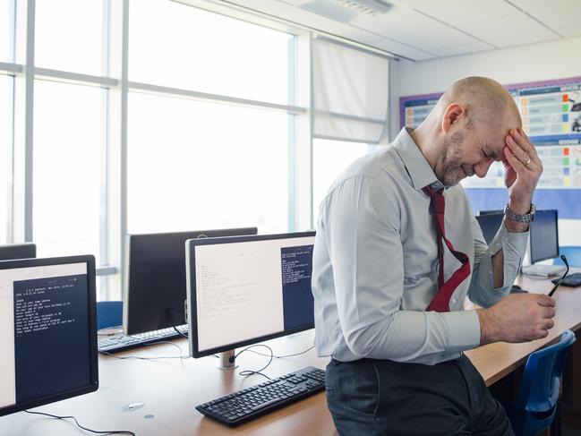 Stressed, concerned teacher sits on the edge of a desk in an empty classroom, schools, upset. Istock