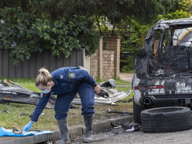 Forensics police officers examine the scene of a burnt out car in Revesby on Sunday. Picture: Monique Harmer